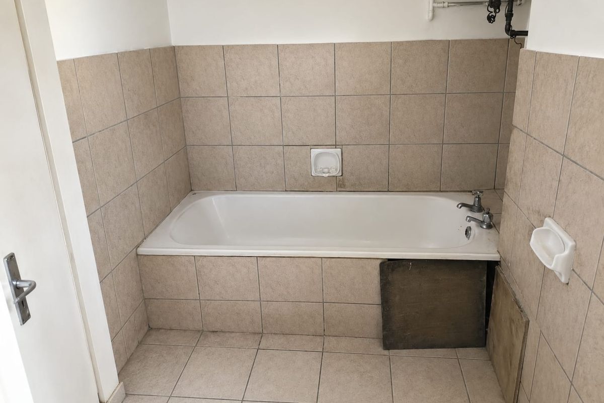 A bathroom featuring a built-in bathtub with ceramic tiling, currently requiring repairs to the bathtub access panel and surrounding tile finish.