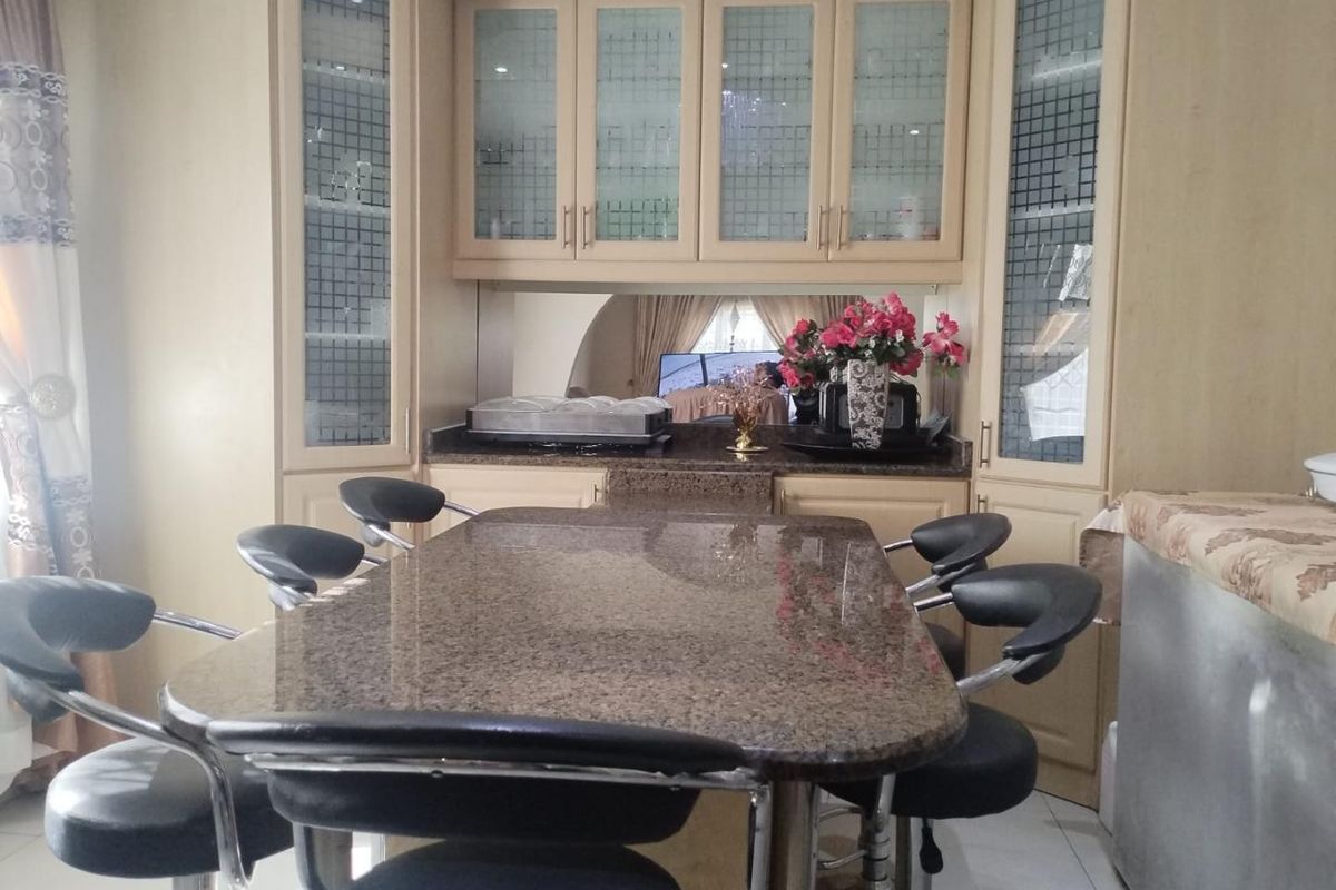 A kitchen area featuring granite countertops, built-in cabinetry with glass-fronted display units, and a mirrored backsplash.