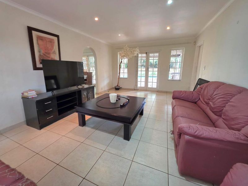 Spacious living room featuring tiled flooring, recessed downlights, and french doors leading to the outdoor area, with an arched entryway to adjacent spaces.