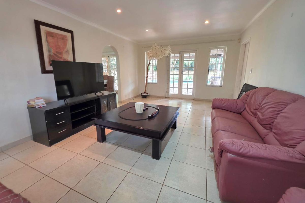 Spacious living room featuring tiled flooring, recessed downlights, and french doors leading to the outdoor area, with an arched entryway to adjacent spaces.
