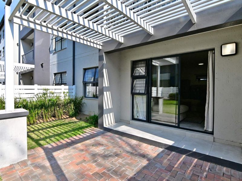 A private ground floor patio featuring brick paving, a modern pergola structure, and direct access to the interior through sliding glass doors.