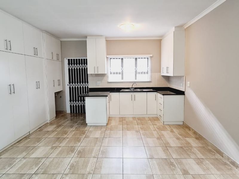 A clean, functional kitchen featuring ample white built-in cabinetry, dark countertops, tiled flooring, and a secure entrance door.