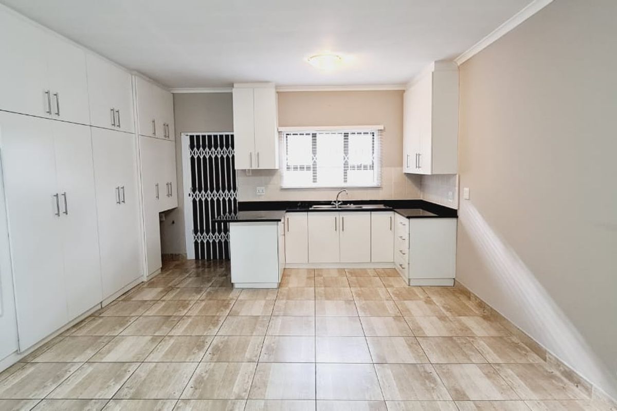 A clean, functional kitchen featuring ample white built-in cabinetry, dark countertops, tiled flooring, and a secure entrance door.