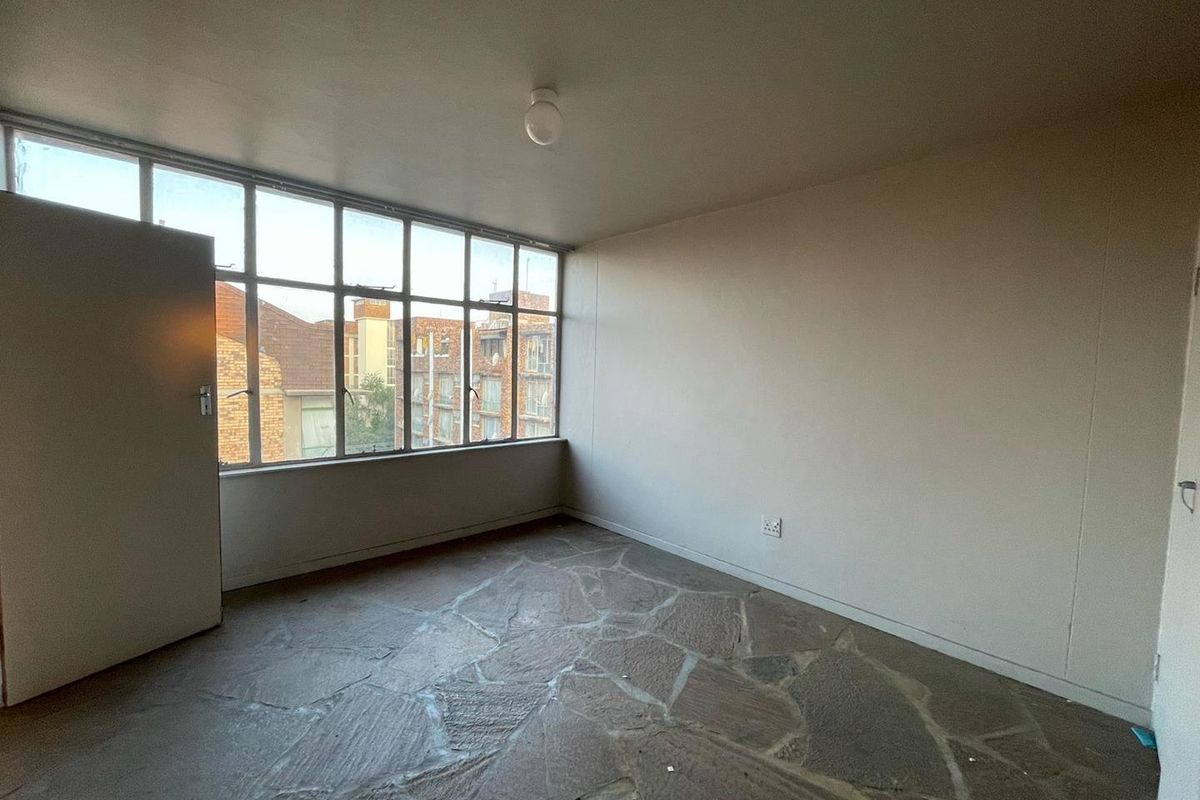 An empty bedroom featuring large metal-framed windows, natural stone flooring, and a simple ceiling light fixture.