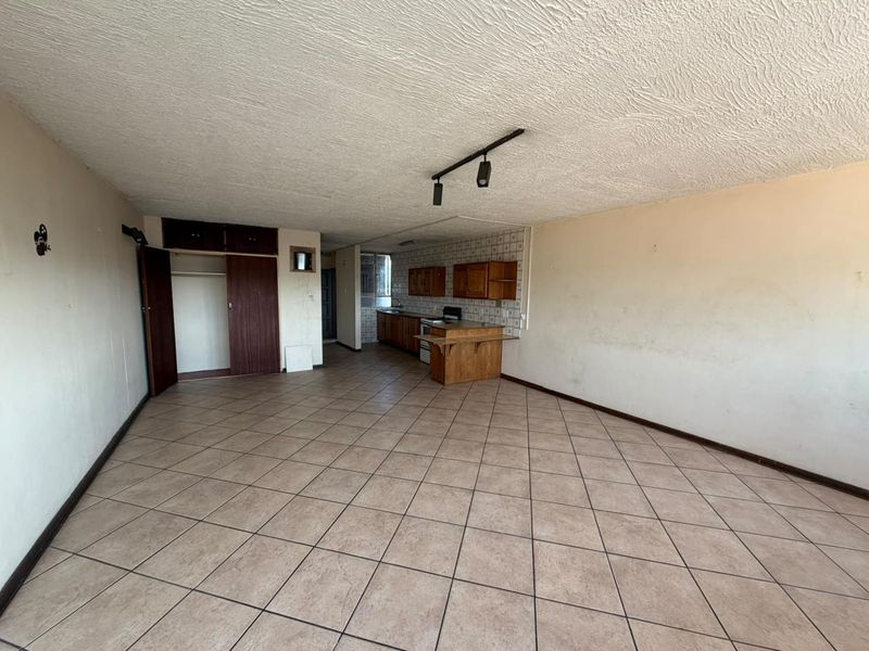 Spacious open-plan living and kitchen area featuring tiled flooring, built-in cabinetry, and track lighting, offering a blank canvas for renovation.
