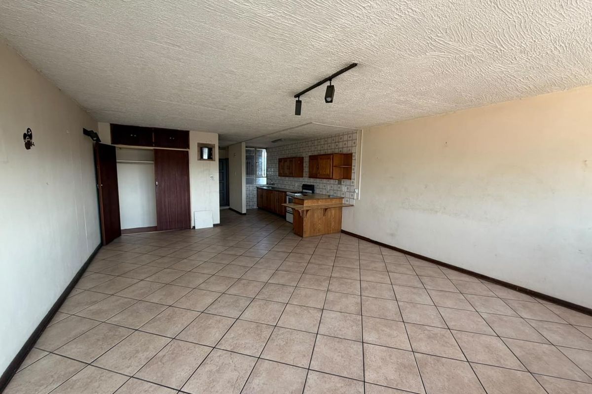 Spacious open-plan living and kitchen area featuring tiled flooring, built-in cabinetry, and track lighting, offering a blank canvas for renovation.