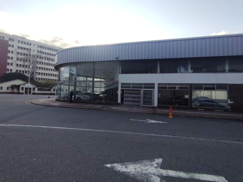 A commercial retail building featuring a prominent curved glass facade and metal roof cladding, situated on a corner lot with street-level access.