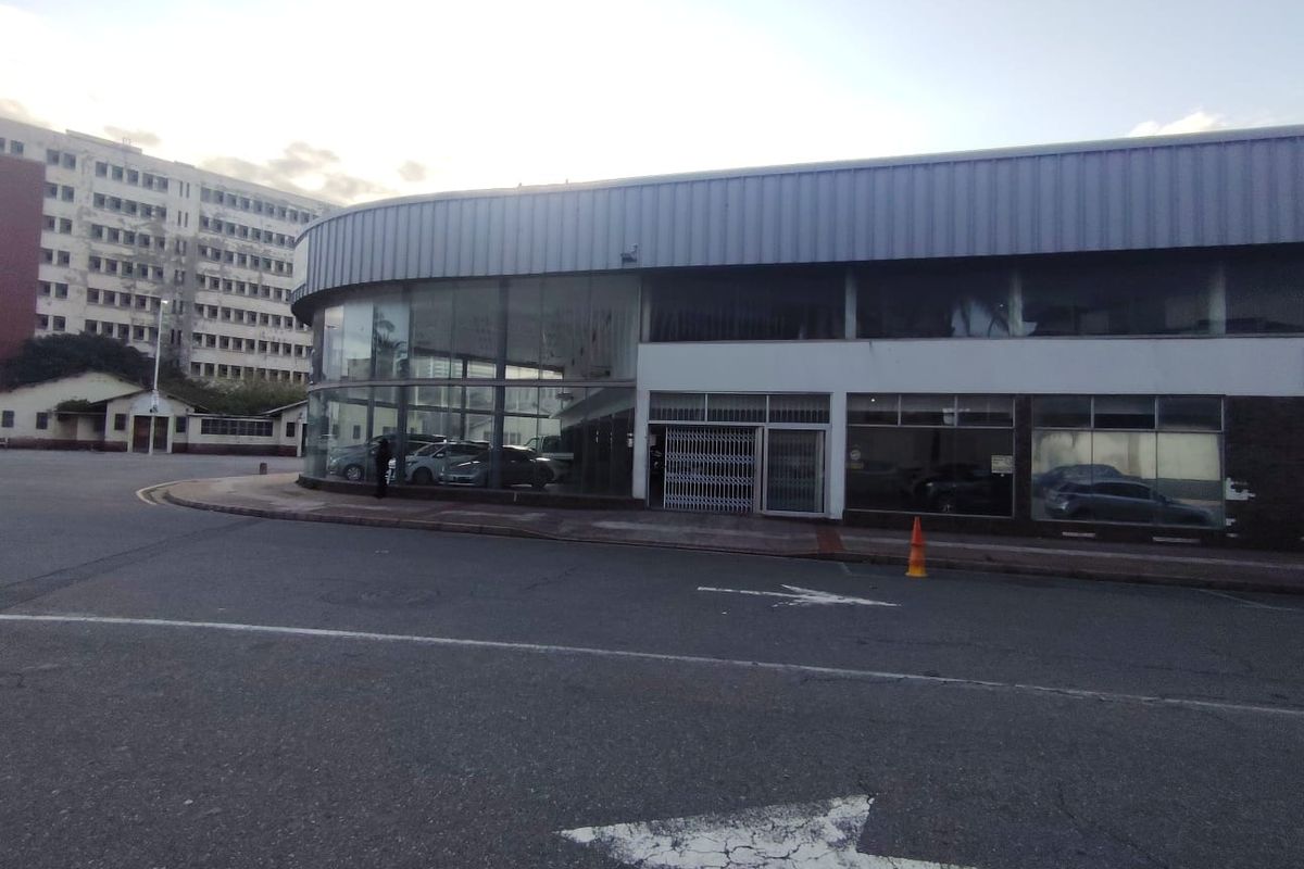 A commercial retail building featuring a prominent curved glass facade and metal roof cladding, situated on a corner lot with street-level access.