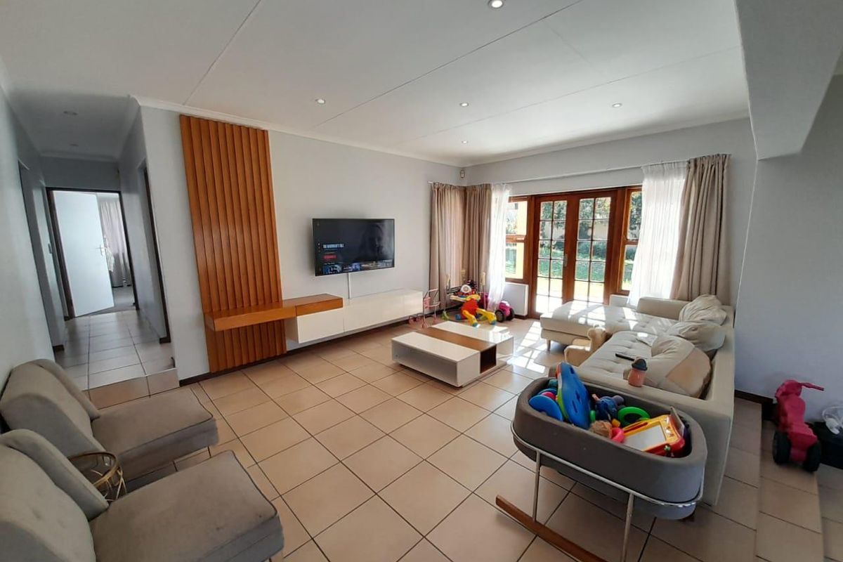 Spacious living room featuring tiled flooring, recessed ceiling lighting, and a built-in wooden feature wall with integrated cabinetry, leading to a garden-facing patio.