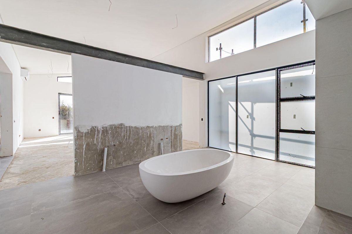 Spacious bathroom under construction featuring a modern freestanding bathtub, large format floor tiles, and expansive windows with frosted glass panels.