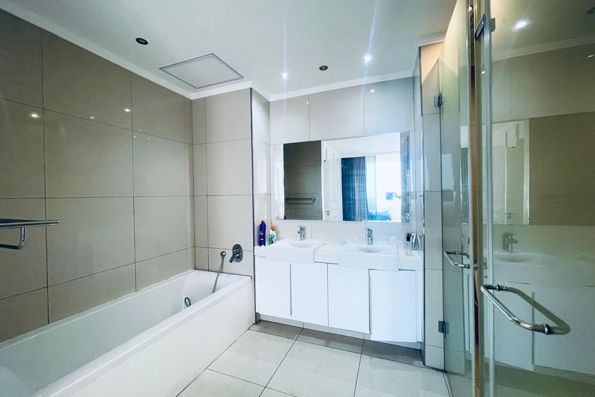 Modern bathroom featuring a double vanity, built-in bathtub, and a separate glass-enclosed shower with neutral floor-to-ceiling tiling.