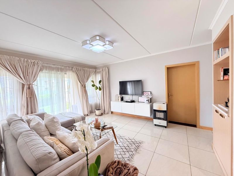 A bright and well-maintained living room featuring large format floor tiles, a built-in shelving unit, and sliding glass doors leading to the exterior.