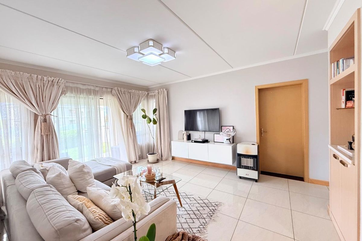 A bright and well-maintained living room featuring large format floor tiles, a built-in shelving unit, and sliding glass doors leading to the exterior.