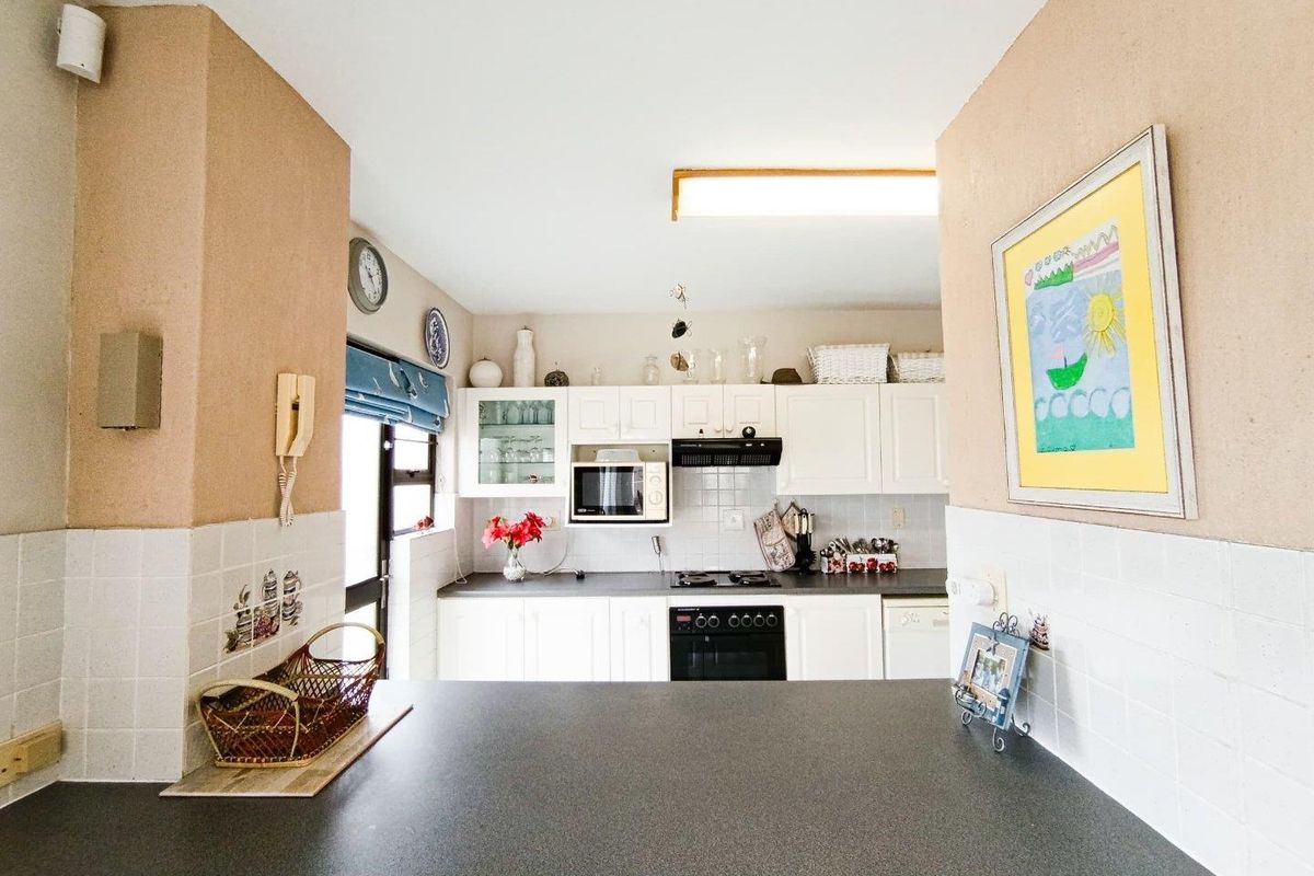 A functional kitchen featuring white cabinetry, dark countertops, a built-in oven, hob, and extractor fan, with a convenient breakfast bar counter.