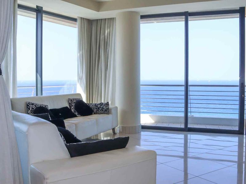 Bright living area featuring floor-to-ceiling glass sliding doors that open onto a balcony with expansive ocean views.