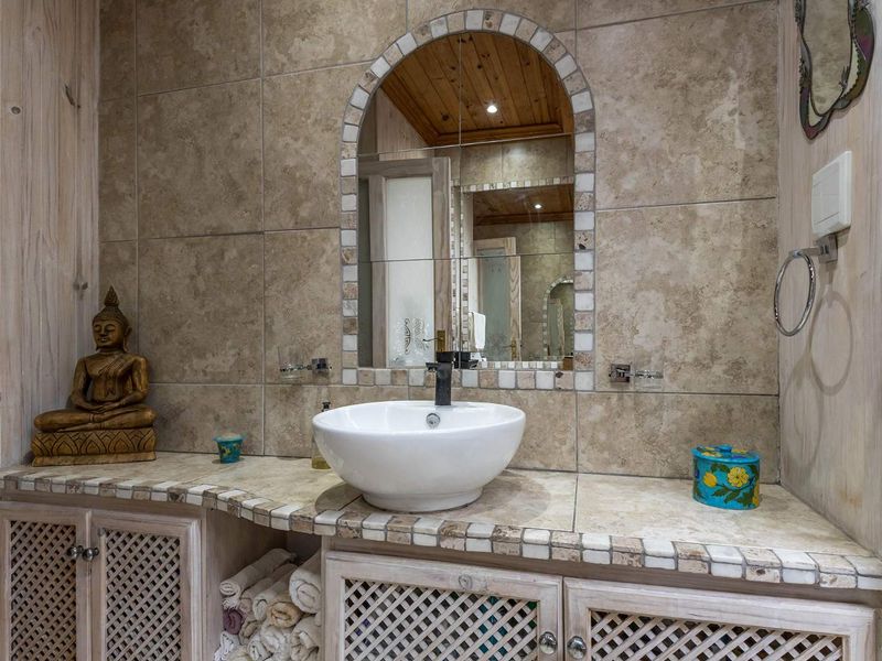 A bathroom vanity area featuring a vessel sink, tiled countertop, built-in cabinetry, and an arched mirror with decorative tile trim.