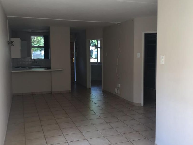 An open-plan living and kitchen area featuring neutral ceramic floor tiles, built-in kitchen cabinetry, and a functional layout ready for personalization.