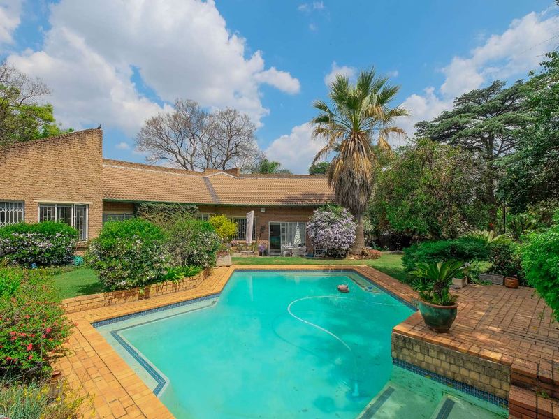 Spacious rear garden featuring a swimming pool with brick surround, established landscaping, and direct access to the main residence.