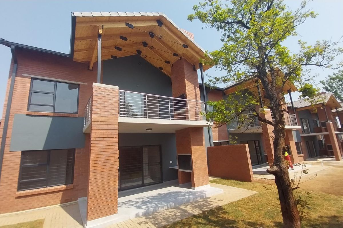 Rear view of a modern townhouse featuring a covered patio with a built-in braai, a balcony with stainless steel railings, and exposed timber roof trusses.
