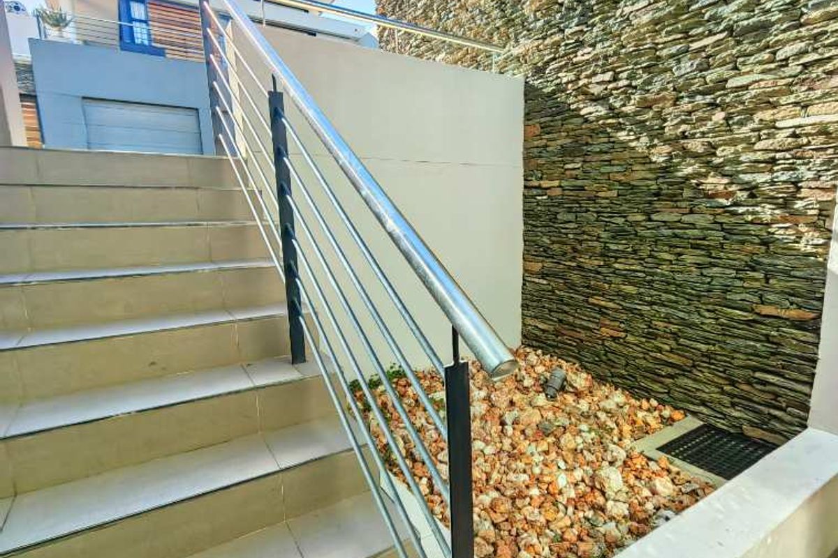 An exterior staircase featuring modern tiled steps, a stainless steel handrail, and a decorative stone cladding wall.