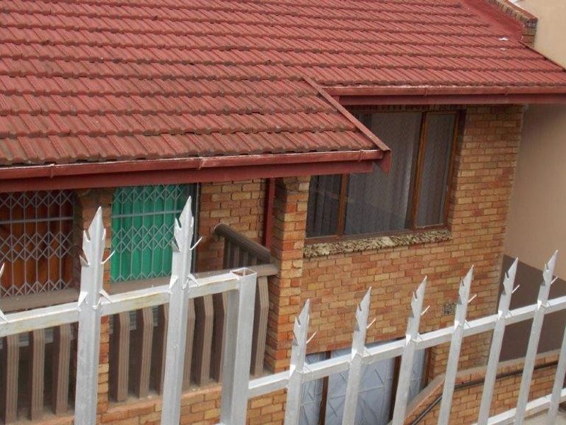 Rear exterior view of a brick house featuring a tiled roof, guttering, and metal security fencing with spikes.