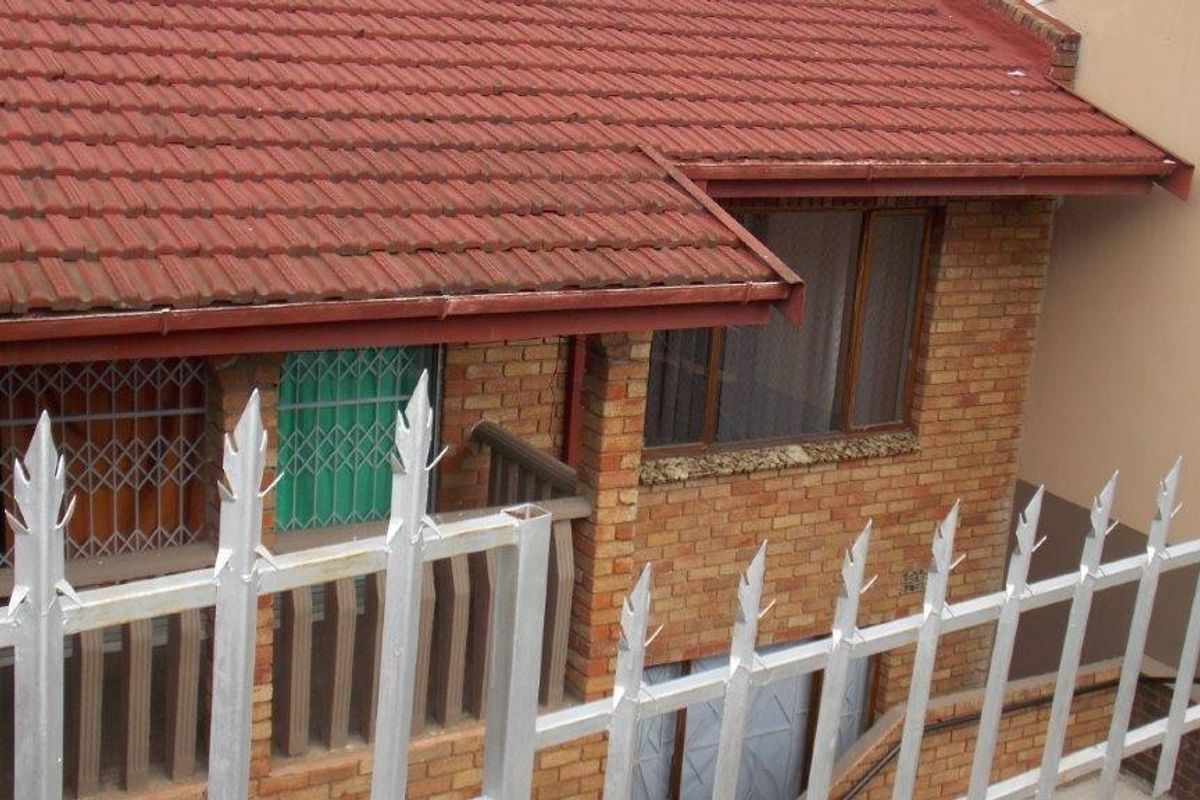 Rear exterior view of a brick house featuring a tiled roof, guttering, and metal security fencing with spikes.