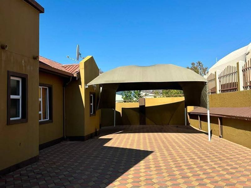 A spacious rear exterior area featuring paved flooring, a shade sail structure, and secure boundary walls.