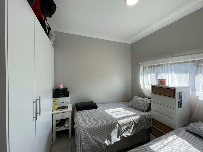 A compact bedroom featuring a built-in wardrobe, tiled flooring, and neutral wall finishes, offering a functional space with natural light.