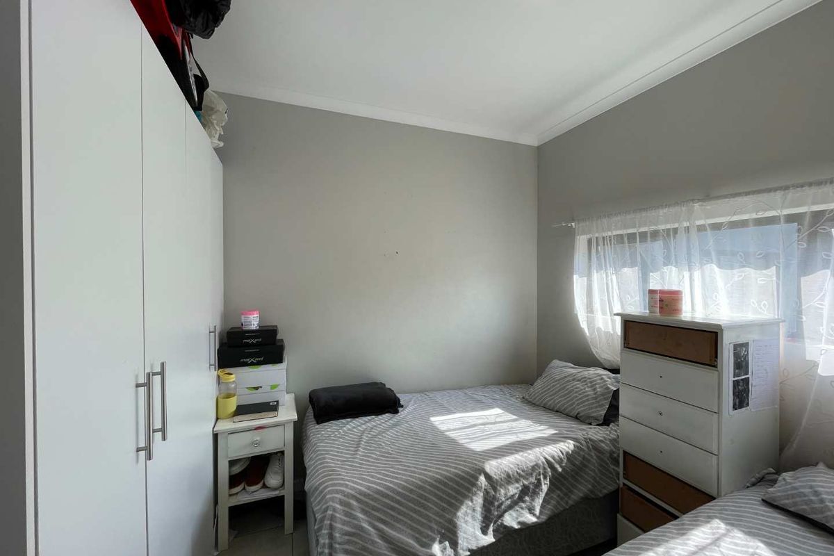 A compact bedroom featuring a built-in wardrobe, tiled flooring, and neutral wall finishes, offering a functional space with natural light.