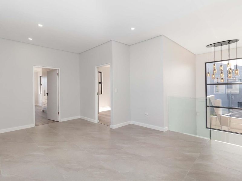 A bright and modern landing area featuring large format floor tiles, a glass balustrade, and contemporary pendant lighting.