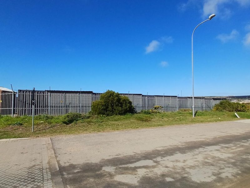 Exterior view of the industrial property featuring secure steel palisade fencing with electric wiring and a paved driveway approach.
