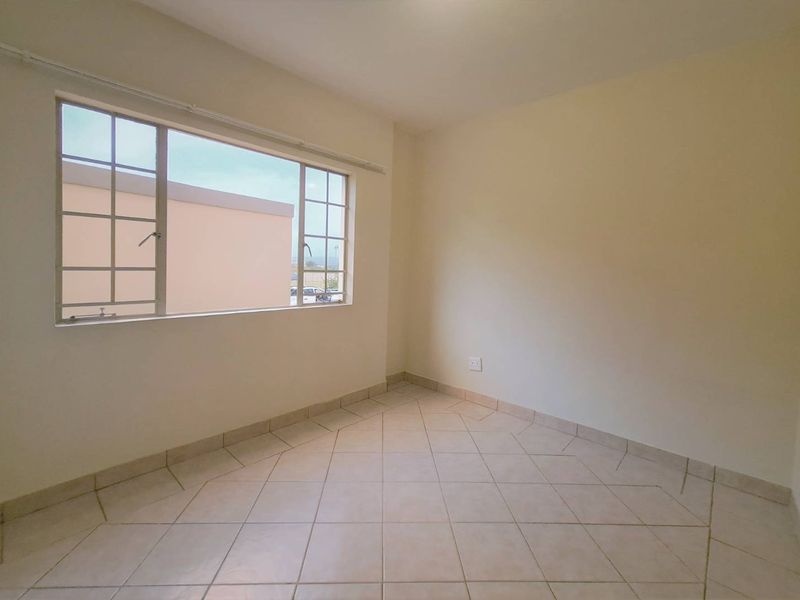 A bright, empty bedroom featuring neutral tiled flooring and a large grid-pattern window, providing a clean canvas for personalization.