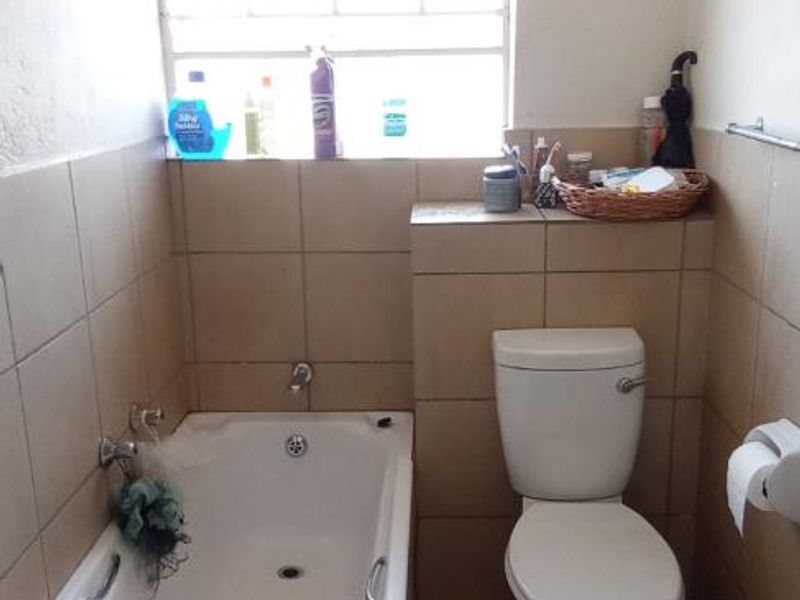 A functional bathroom featuring a bathtub, toilet, and tiled finishes, with an exposed electric water heater unit.