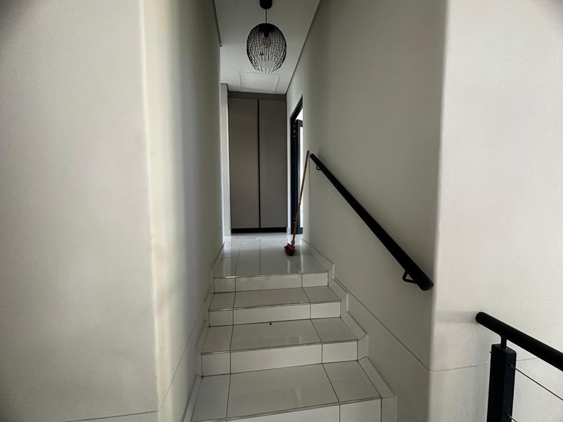 A clean, modern hallway featuring a tiled staircase with a black handrail and a built-in storage cupboard at the landing.
