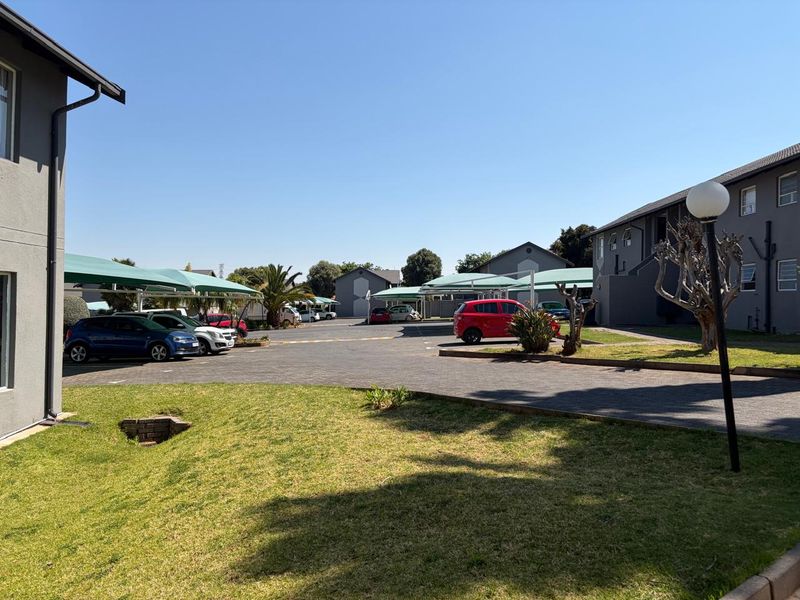Exterior view of the townhouse complex featuring a paved parking area with shade sail carports and surrounding landscaped grounds.