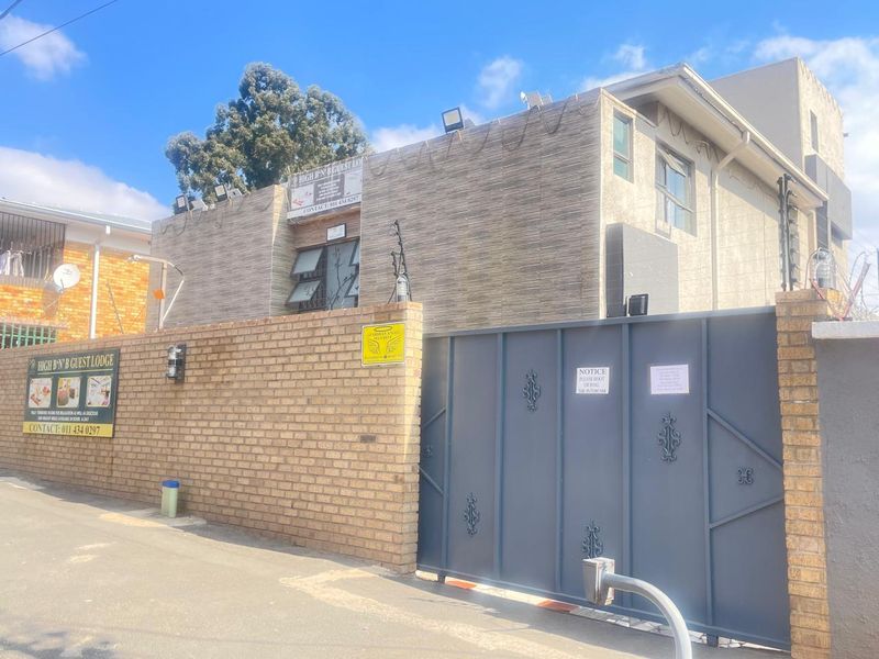 Front exterior view of the guest house featuring a brick boundary wall, secure metal gate, and integrated security systems.
