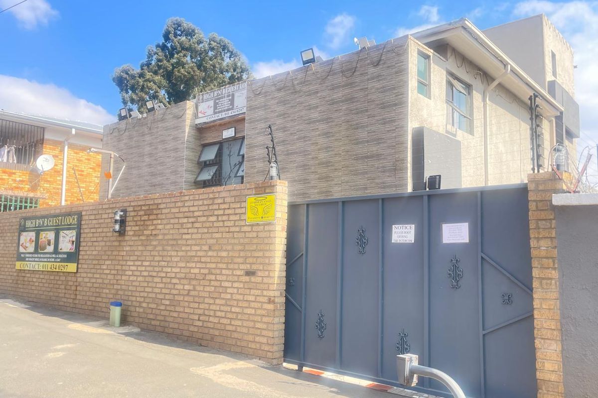 Front exterior view of the guest house featuring a brick boundary wall, secure metal gate, and integrated security systems.