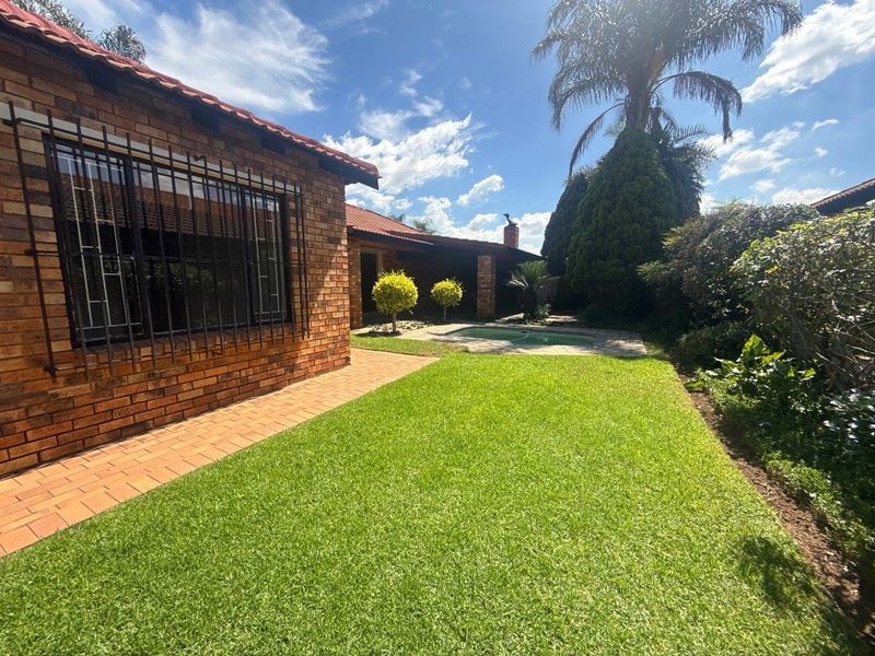 Rear view of the townhouse featuring a brick facade, a well-maintained lawn, and a private swimming pool area.
