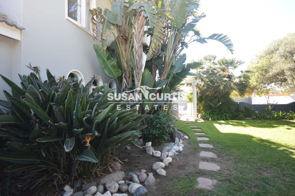 A view of the rear garden featuring a stone pathway, established tropical landscaping, and a structural archway leading to the outdoor area.