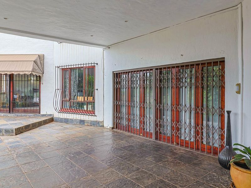 A spacious covered patio area featuring tiled flooring, security gates, and sliding glass doors, providing a functional outdoor entertainment space.