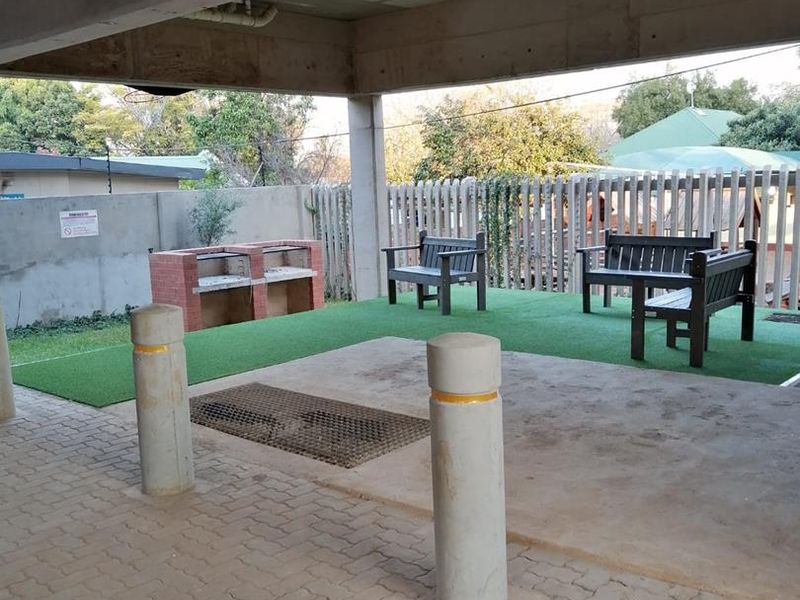 A covered outdoor patio area featuring a built-in brick braai, paved flooring, and artificial grass, suitable for communal or private outdoor entertainment.