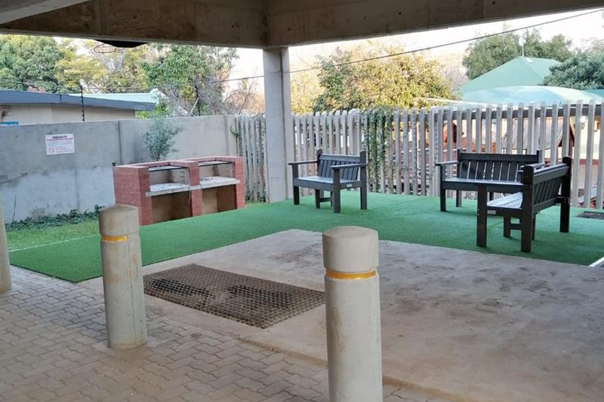 A covered outdoor patio area featuring a built-in brick braai, paved flooring, and artificial grass, suitable for communal or private outdoor entertainment.