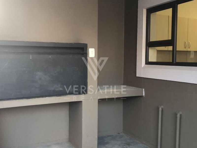 Covered patio area featuring a built-in braai, concrete prep counter, and direct window access to the kitchen.