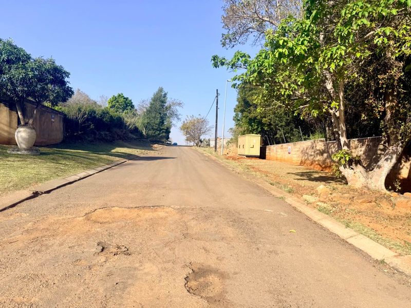 A view of the residential street frontage showing the asphalt road surface, boundary walls, and utility infrastructure.