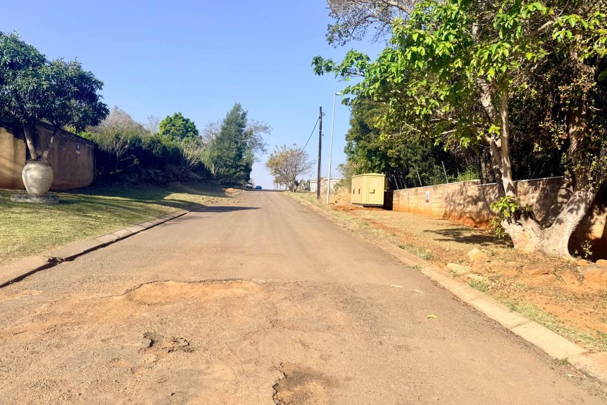 A view of the residential street frontage showing the asphalt road surface, boundary walls, and utility infrastructure.
