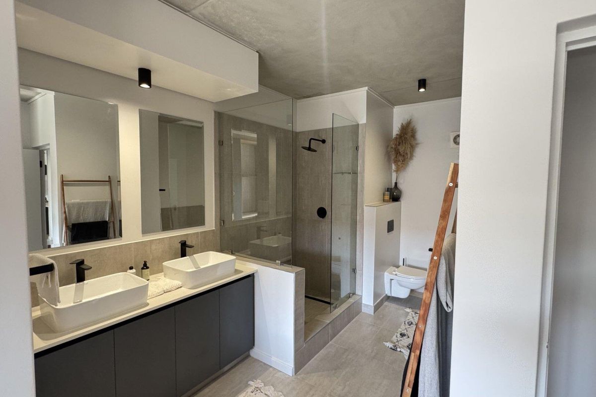 Modern bathroom featuring a double vanity with vessel sinks, matte black fixtures, a walk-in glass shower, and a wall-mounted toilet.