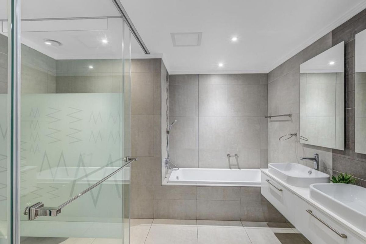 Modern bathroom featuring a double vanity, a built-in bathtub, and a separate glass-enclosed shower with contemporary grey tiling.