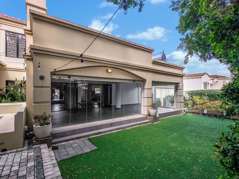 Rear view of the property featuring a paved patio area, artificial lawn, and modern stacking glass doors leading into the living space.