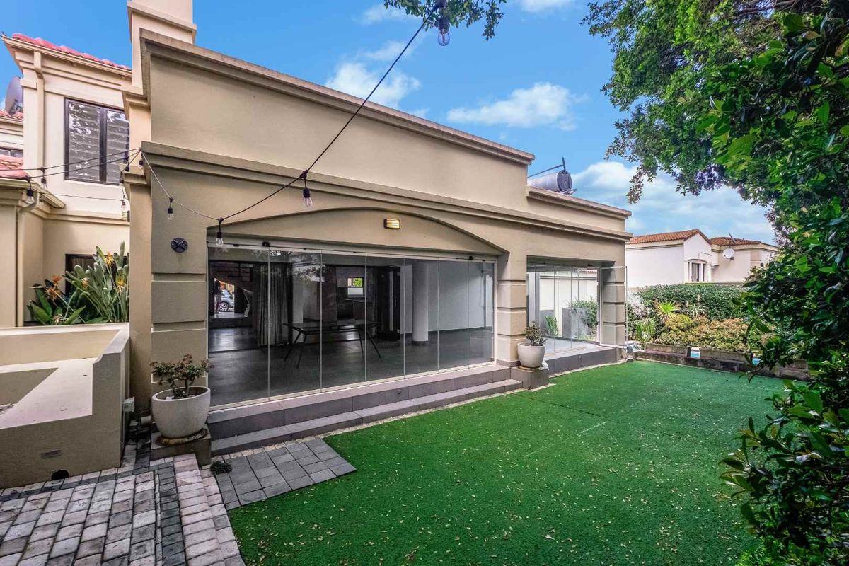 Rear view of the property featuring a paved patio area, artificial lawn, and modern stacking glass doors leading into the living space.