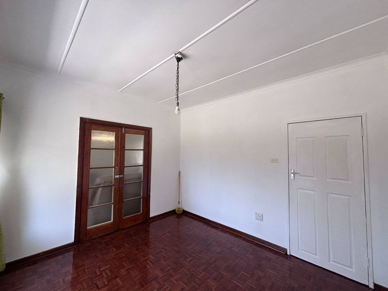 An empty living room featuring polished parquet flooring, classic wooden french doors, and a simple coved ceiling, offering a clean canvas for interior design.